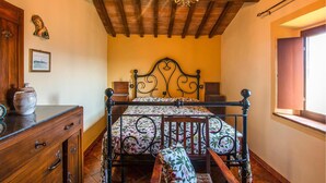 A bedroom with a wooden ceiling, a bed with a floral bedspread, a wooden dresser, a vase, and a framed picture on the wall. - Lovely apartment in Volterra with WiFi (Volterra)
