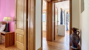 Un couloir avec des portes en bois, une table de chevet avec une lampe et un vase posé sur le sol.