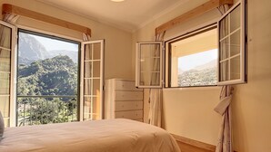 Une chambre à coucher avec un lit, une commode et deux fenêtres dont les volets sont ouverts.