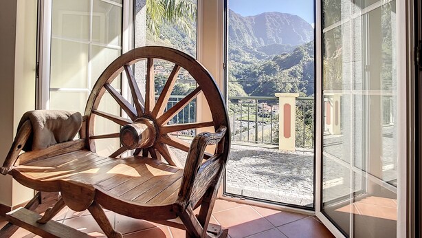 Une table en bois, un grand fauteuil roulant, une porte en verre et une vue sur les montagnes et une ville.