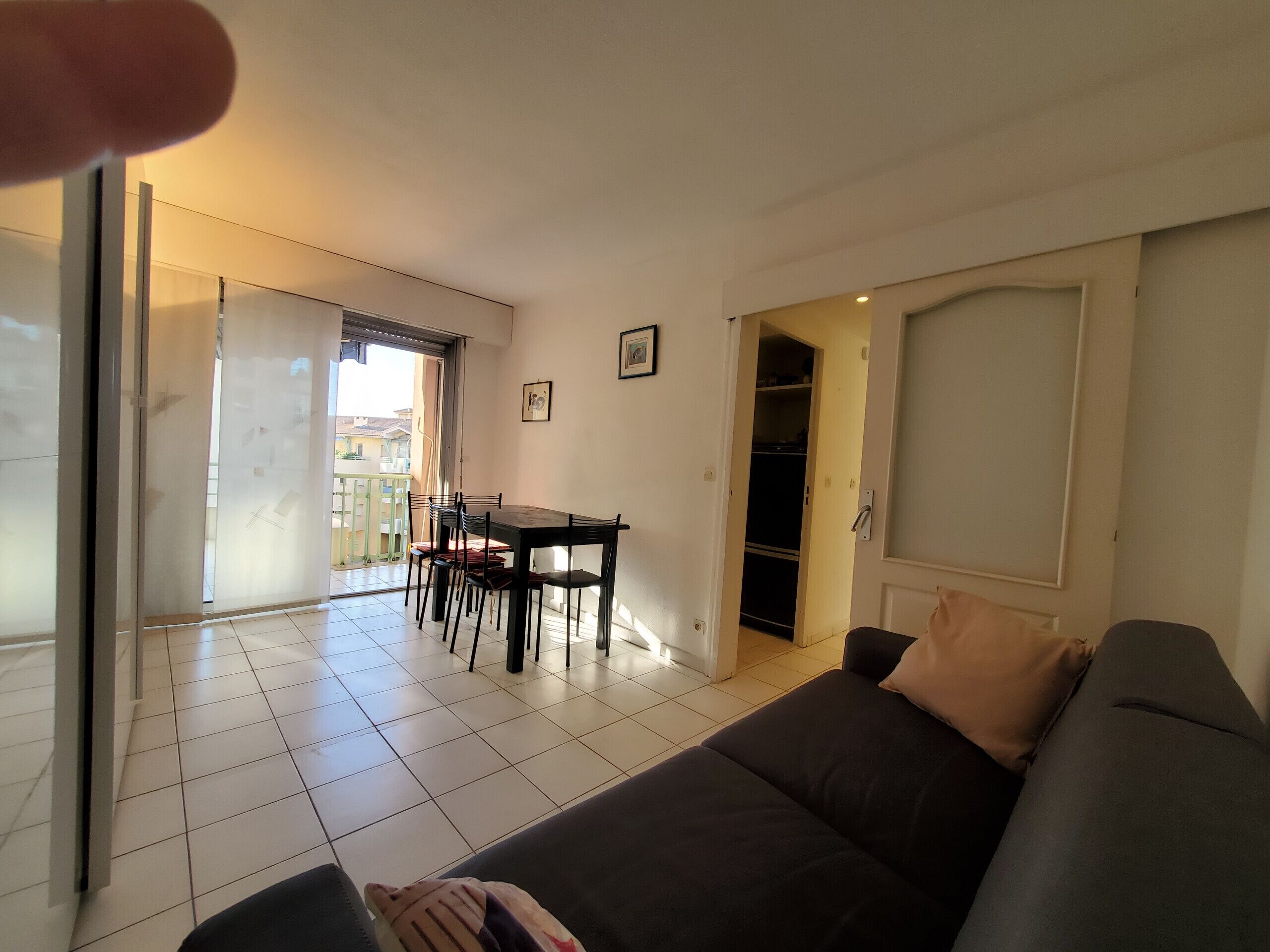 Una sala de estar con un sofá, una mesa de comedor con sillas, un puerta corrediza de vidrio que da a un balcón y un armario con puerta.