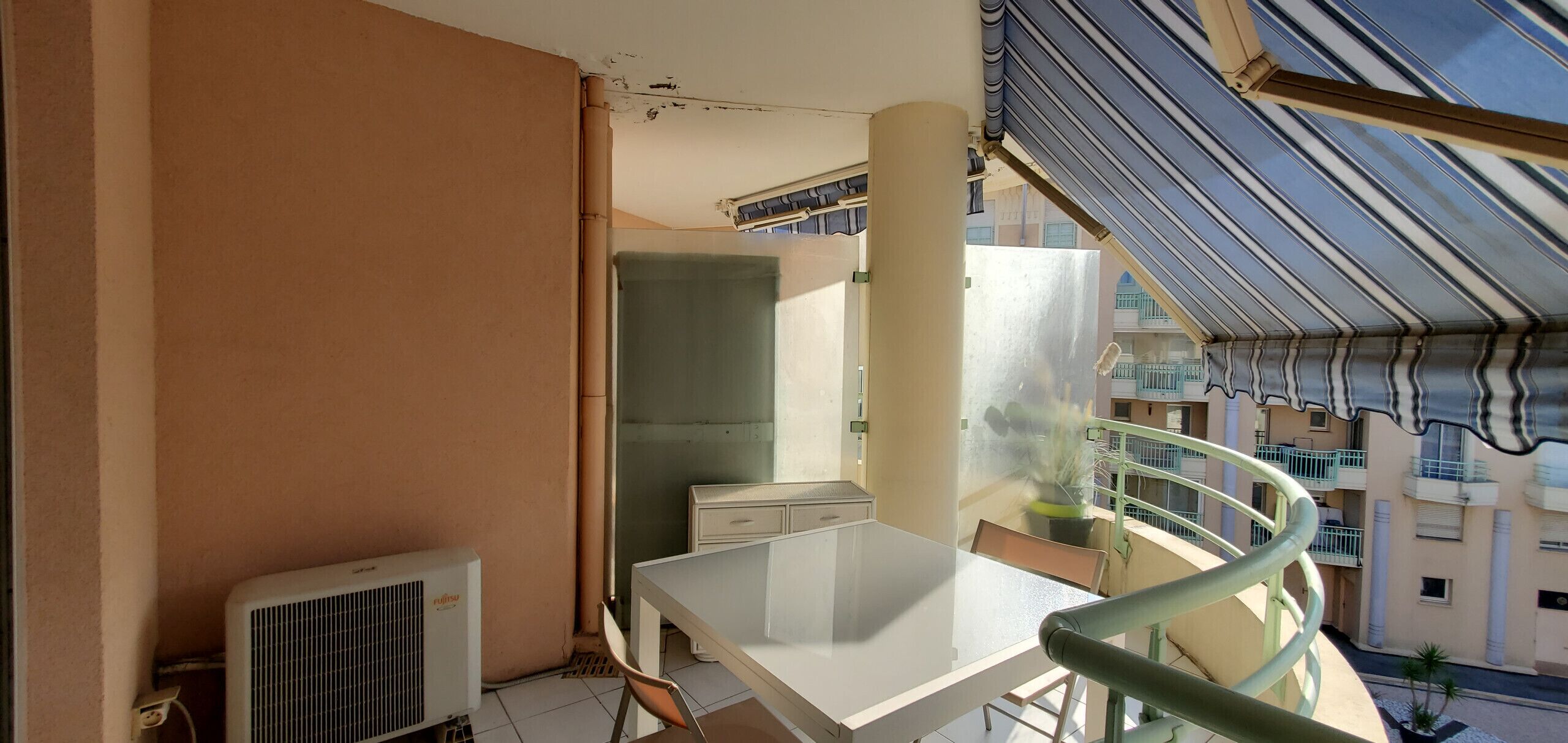 A balcony with a table and chairs, a radiator, and a view of neighboring buildings.
