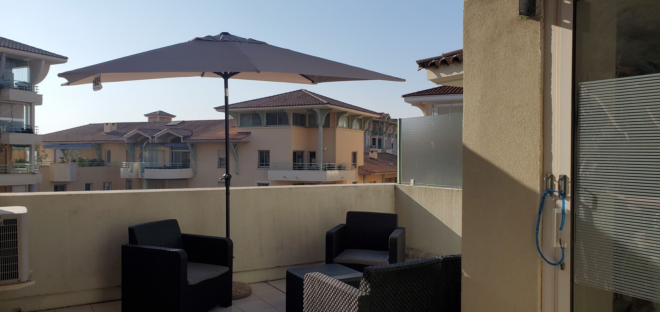 En balkon med udendørs møbler, en stor parasol og udsigt til omkringliggende bygninger.