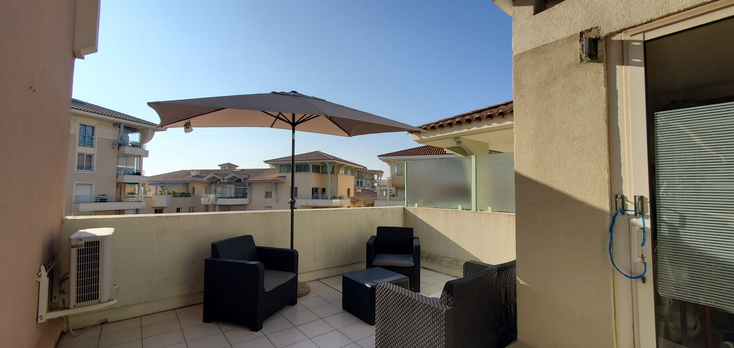 A balcony with outdoor furniture, including two chairs and a table, under a large umbrella.