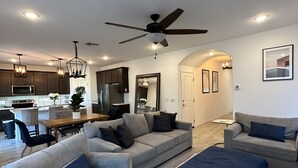 Un salon moderne avec un canapé gris, un pouf bleu et un coin repas comprenant une table et des chaises en bois.
