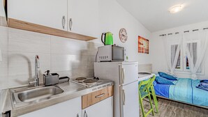 A compact kitchen with a sink, stove, and microwave. There is a bed with a blue and white striped bedspread and a green chair. - Gorgeous home in Potomje with WiFi (Potomje)