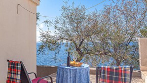 A terrace with a table set for two, overlooking a body of water and a tree with sparse foliage. - Gorgeous home in Potomje with WiFi (Potomje)