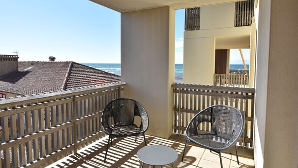 Un balcon avec deux fauteuils en osier et une petite table, donnant sur la mer.