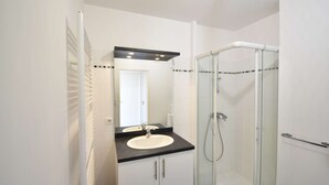 Une salle de bain moderne avec une douche à parois de verre, un lavabo blanc et un plan de toilette noir.