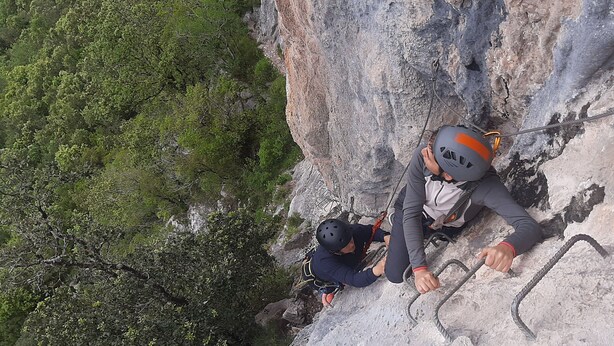 A person climbing a rocky cliff with a rope.