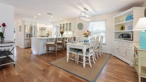 A spacious kitchen with a dining area, wooden flooring, and white cabinetry. - Bay 2 Bay: Bay Across Street! Amazing Views of Bay & Canal, Pool & Lounge by Anna Maria Life (Anna Maria)