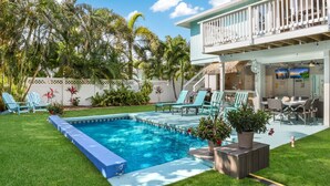 A pool area with a blue pool, green lawn, and outdoor seating with chairs and tables. - Bay 2 Bay: Bay Across Street! Amazing Views of Bay & Canal, Pool & Lounge by Anna Maria Life (Anna Maria)
