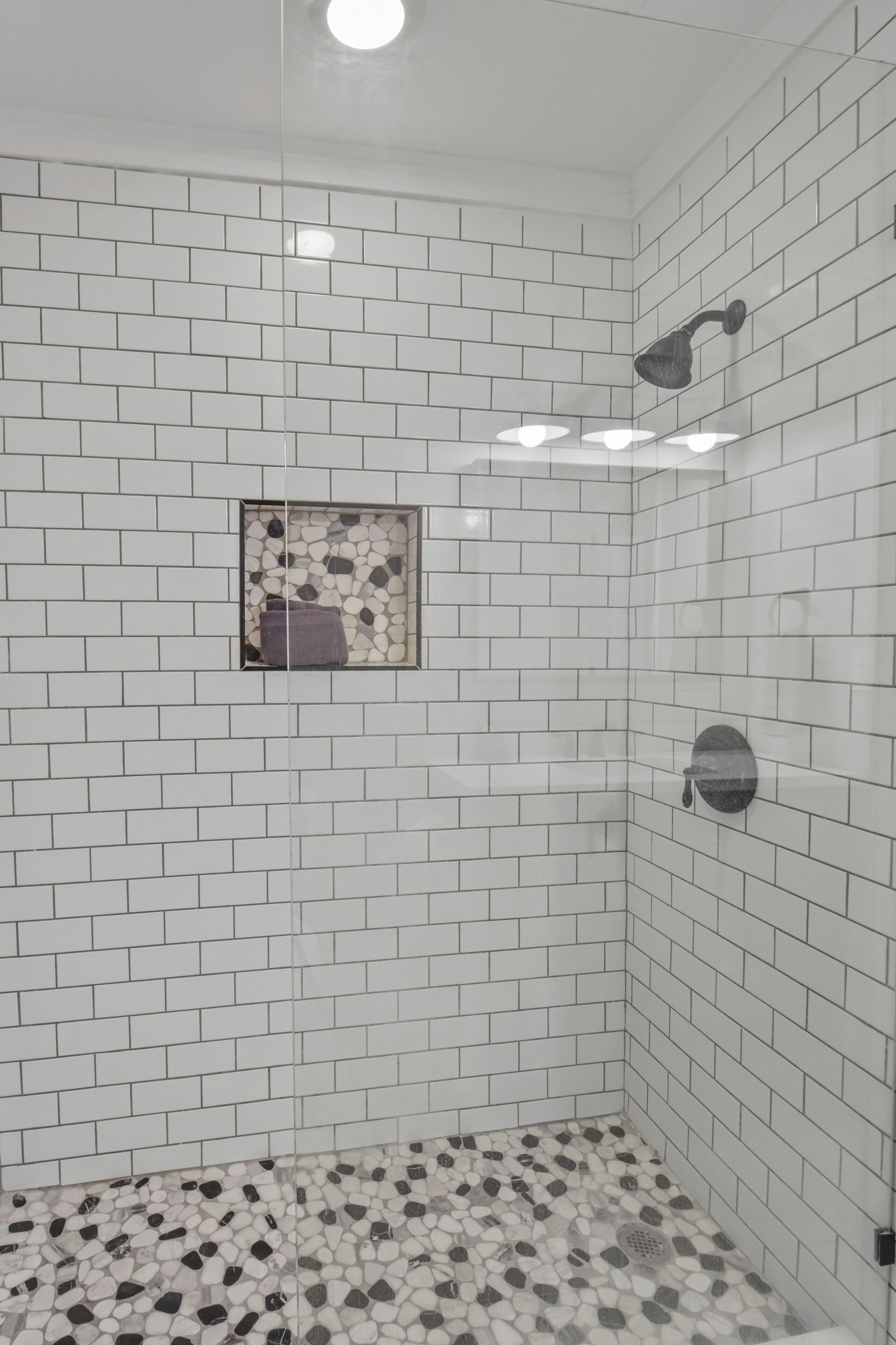 Eine Dusche mit weiß gefliesten Wänden und einem Boden mit Kieselmuster.