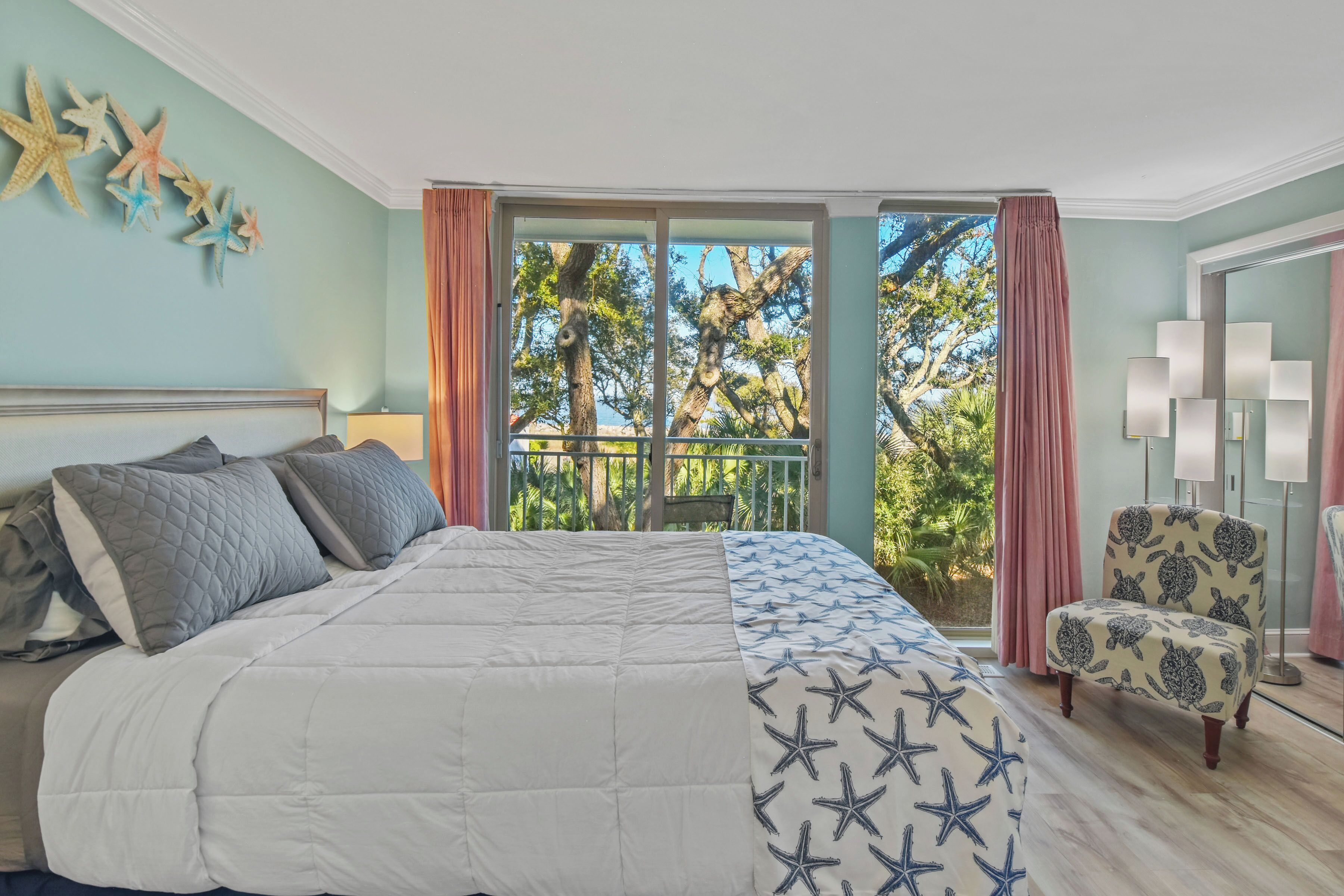 Une chambre avec un lit, une chaise, un balcon avec des rideaux et une vue sur les arbres.