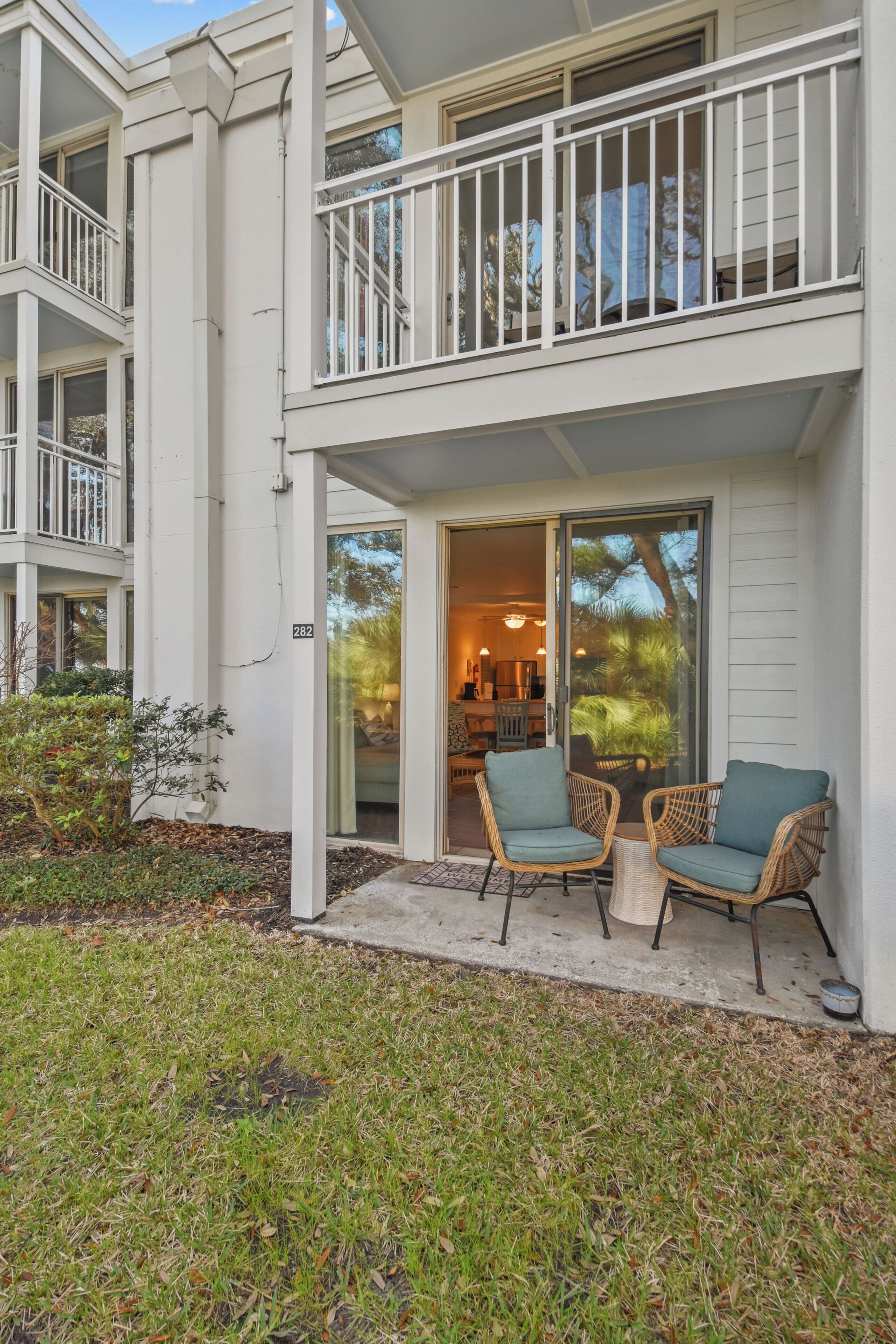 A two-story building with a balcony, a covered patio with wicker furniture, and a visible interior with a dining area.