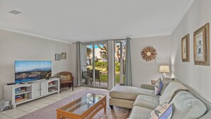 A living room with a sofa, TV, entertainment unit, and a view through a glass door.