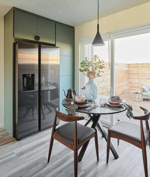 Une cuisine moderne avec un réfrigérateur en acier inoxydable, une table à manger avec deux chaises et un vase de fleurs posé sur la table.