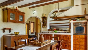 A traditional kitchen with wooden cabinets, a dining table, chairs, and a built-in oven. - Villa TreA - Loft Alba (Mascali)