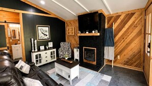 A modern living room with a leather sofa, a fireplace, a television, and a patterned armchair. - Fish Cabin at the Pines - Lake O' the Pines - Hot Tub - Fire Pit (Jefferson)