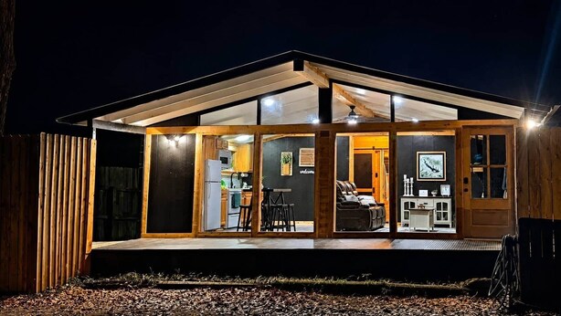 A modern house with a glass front, wooden exterior, and a well-lit interior. - Fish Cabin at the Pines - Lake O' the Pines - Hot Tub - Fire Pit (Jefferson)