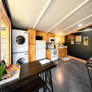 A modern kitchen with wooden cabinets, a washing machine, a refrigerator, a microwave, and a stove. - Fish Cabin at the Pines (Jefferson)