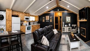 A loft-style living space with a kitchen, a black leather sofa, and a fireplace. - Fish Cabin at the Pines - Lake O' the Pines - Hot Tub - Fire Pit (Jefferson)