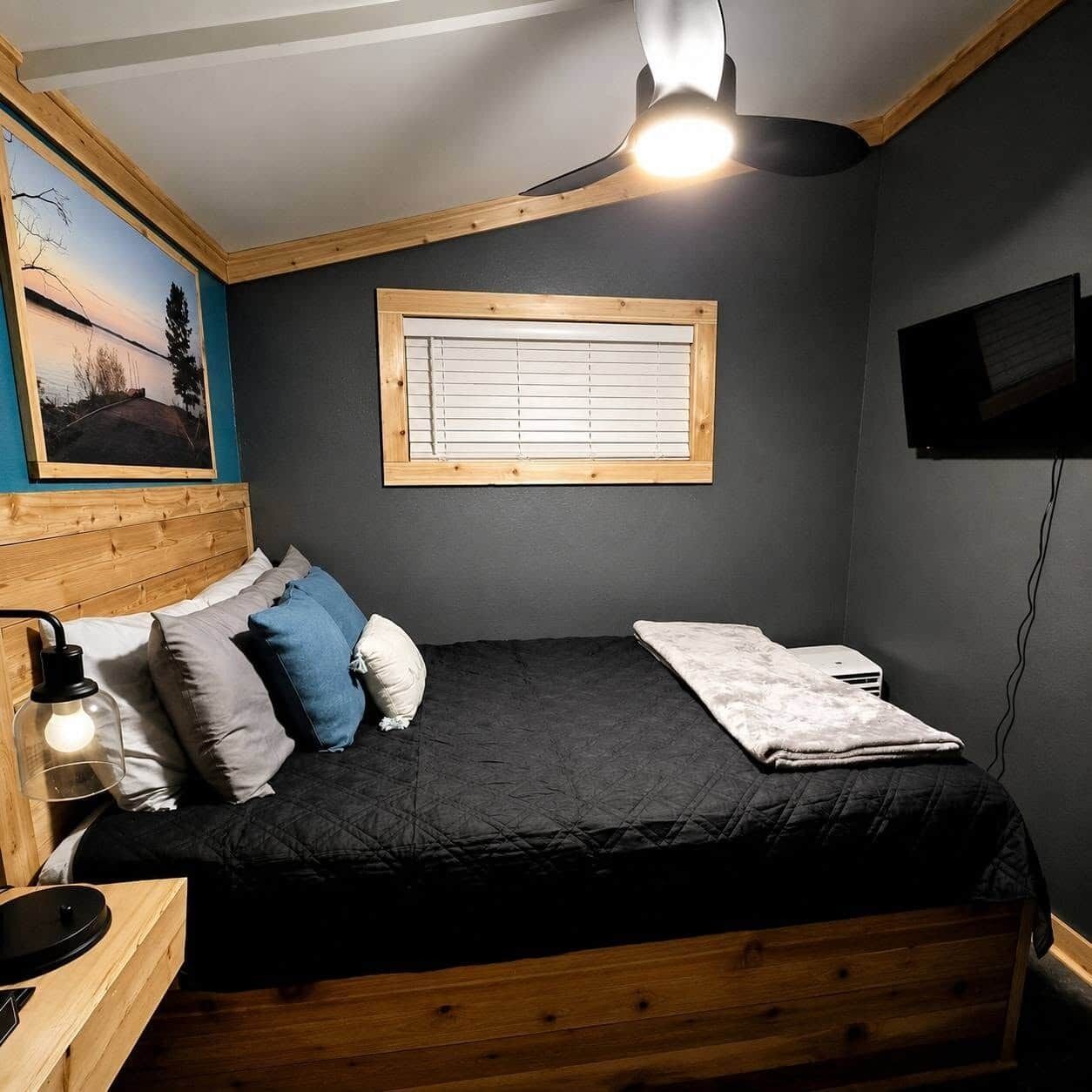 Una camera da letto con un letto, una finestra con persiane, una TV a parete e una lampada a sospensione.