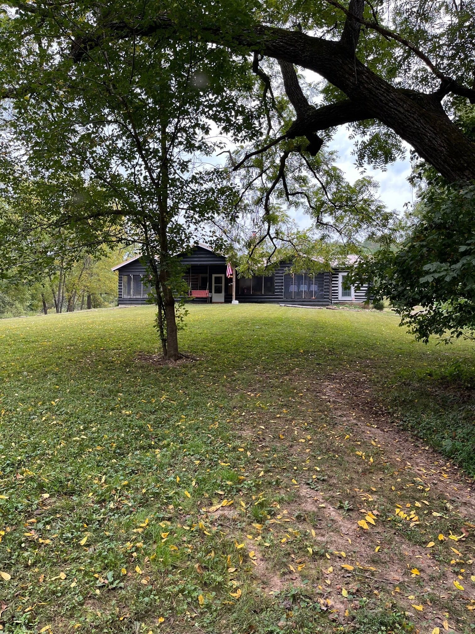 Une cabane dotée d’une véranda et d’un mât pour drapeau, entourée d’une pelouse parsemée de feuilles.