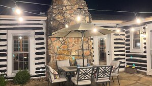 Une terrasse extérieure avec un sol en pierre, une cheminée en pierre et une table avec des chaises.