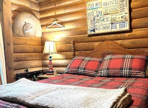 A wooden cabin-style room with a bed, a lamp, and a wall displaying various license plates.