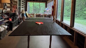 L’intérieur d’un chalet en bois, avec une table de ping-pong, de grandes fenêtres et un luminaire au plafond.
