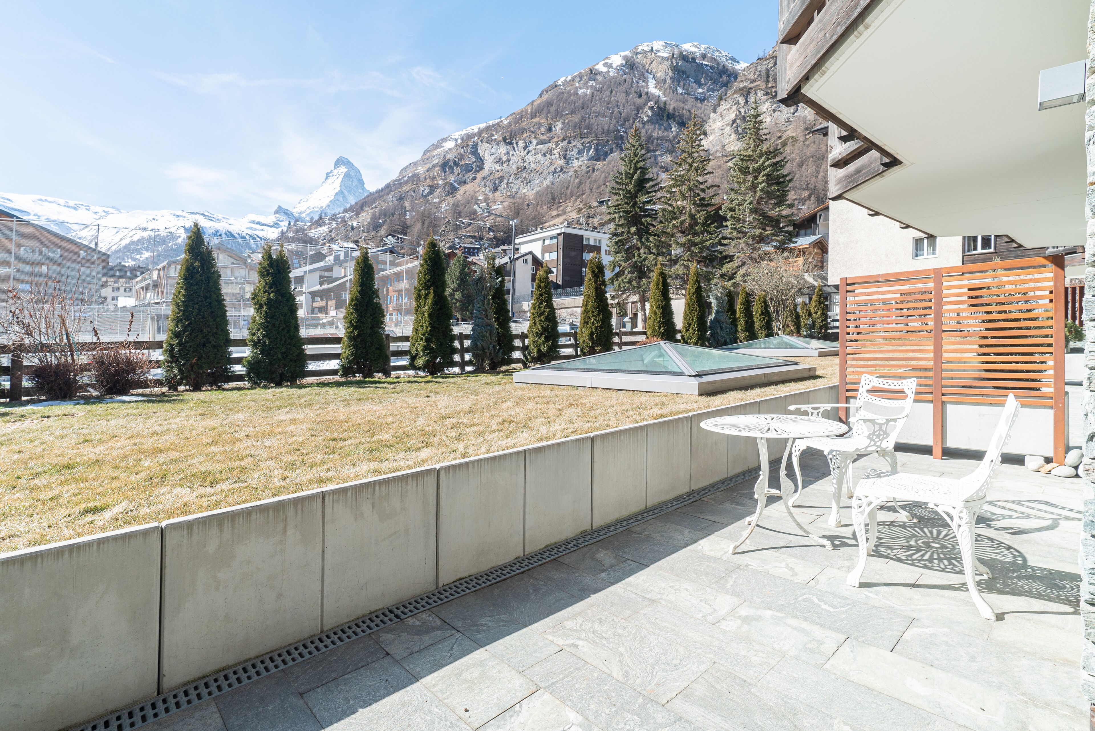 Una terraza con vistas a las montañas, un muro de hormigón y mobiliario exterior.