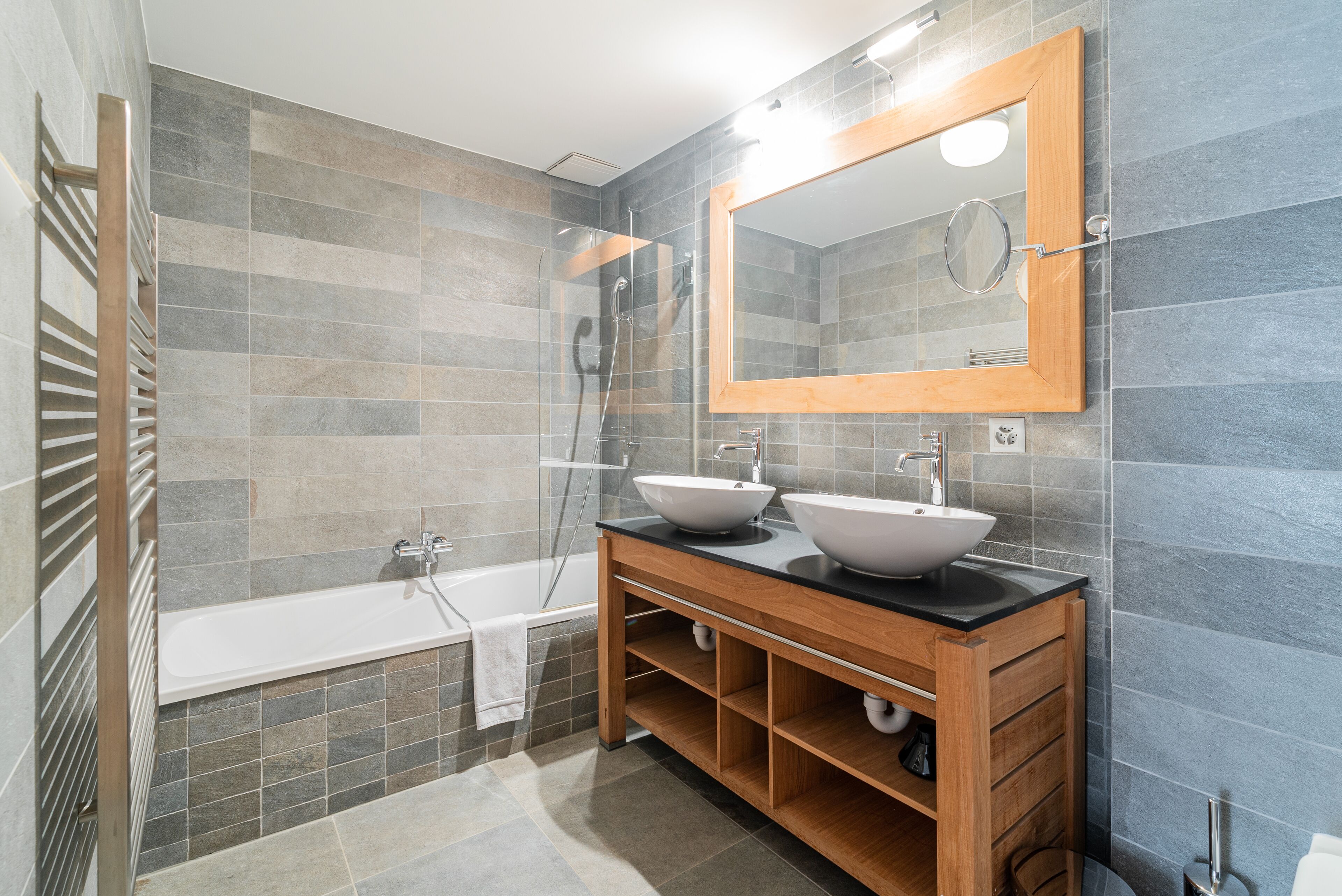 A modern bathroom with two sinks, a large mirror, a bathtub, and a shower.