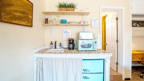 Una cocina equipada con cafetera integrada, microondas y un refrigerador pequeño. Hay repisas sobre la encimera con varios utensilios de cocina.
