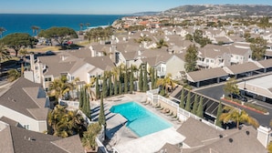 A residential area with a swimming pool surrounded by houses, palm trees, and a view of the ocean. - LOWER Unit at Niguel Beach Terrace, Dana Point!  Close to Pool  view (Dana Point)
