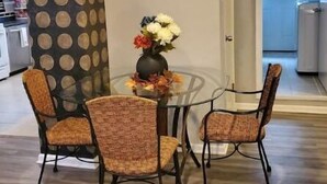 A dining area with a glass table, four wicker chairs, and a vase with flowers.