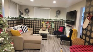 A cozy living room with a beige sofa, a small table, and a TV mounted on the wall.