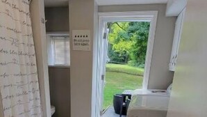 A narrow hallway leading to a bathroom with a toilet and a shower curtain. There is a sign on the wall and a door leading outside.