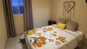 A bedroom with a bed, a hanging light fixture, a wall-mounted air conditioner, and a view through a window with curtains. - Rouse's House near Hotel Zone, Zamna Fest (Tulum)