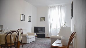 A living room with a sofa, a TV, a dining table with chairs, and a window with curtains. - Casa Cavour by Wonderful Italy (Bellagio)