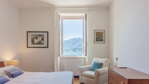 A bedroom with a bed, a chair, a dresser, and a window with a mountain view. - Casa Cavour by Wonderful Italy (Bellagio)