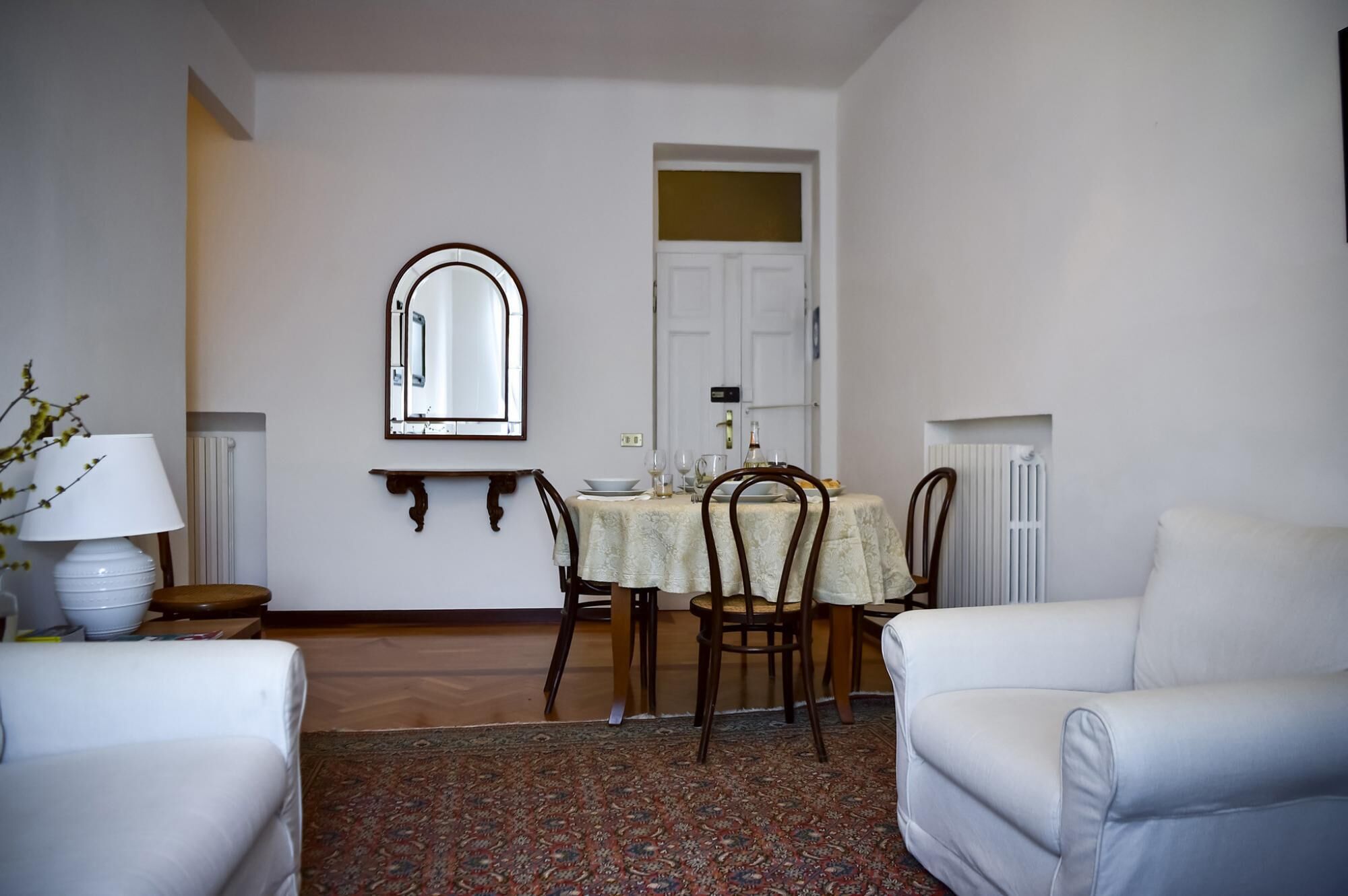 A dining area with a table set for four, a mirror above the table, and a white sofa in the foreground.