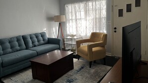 Uma sala de estar com sofá, poltrona, mesa de centro, luminária e televisão.