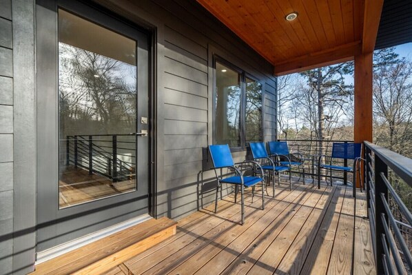 A wooden deck with blue chairs, a glass door, and a view of trees. - Northwoods Contemporary w/ POOL and HOT TUB! (Hot Springs)