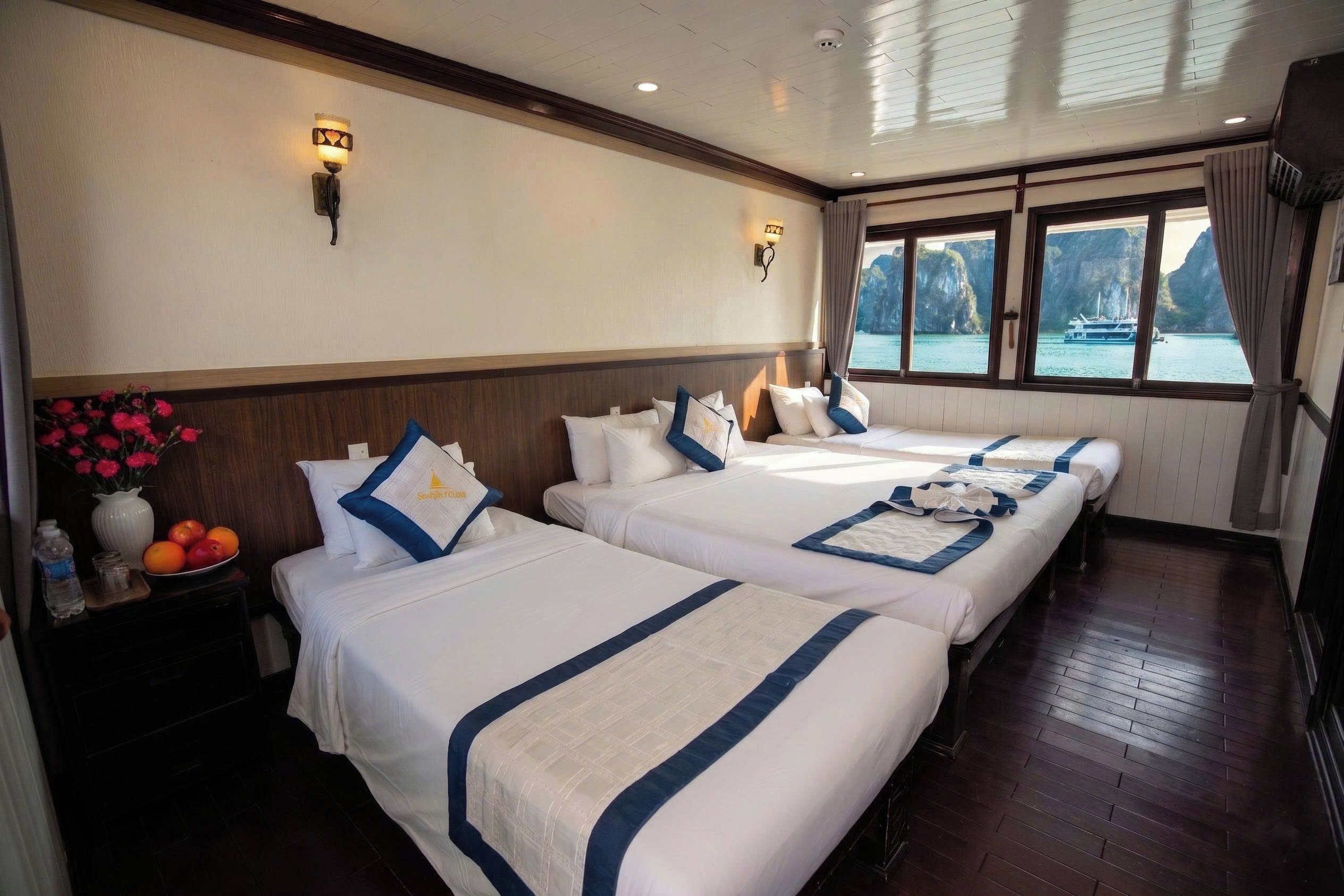 Habitación de hotel con dos camas, una mesita de noche con un florero y vista al mar a través de amplias ventanas.