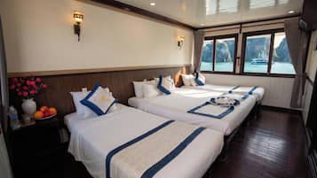 Habitación de hotel con dos camas, una mesita de noche con un florero y vista al mar a través de amplias ventanas.