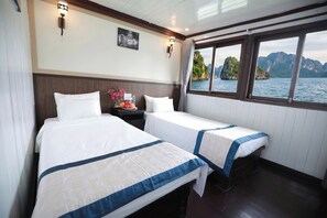 Habitación de hotel con dos camas, una mesita de noche con un florero y una ventana que ofrece vistas a una costa montañosa.