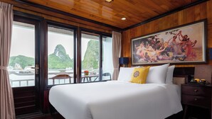 Hotelkamer met een groot bed, een schilderij aan de muur en uitzicht op een boot en bergen door de ramen.