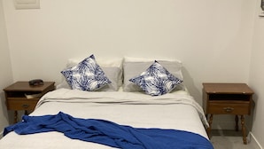 Une chambre à coucher comprenant un lit, deux tables de chevet, un climatiseur fixé au mur et un interrupteur mural.