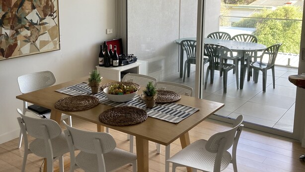 Un coin repas avec une table en bois, des chaises blanches et une vue sur l’extérieur grâce à de grandes portes-fenêtres coulissantes.
